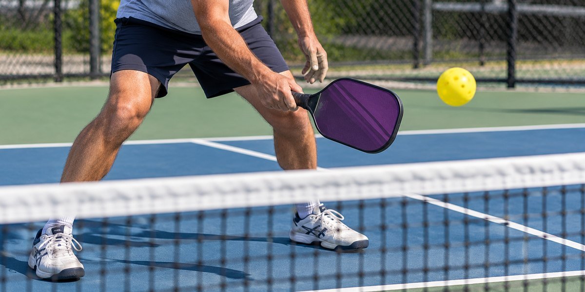 Player in a ready stance at the net holding a purple paddle as the ball comes over