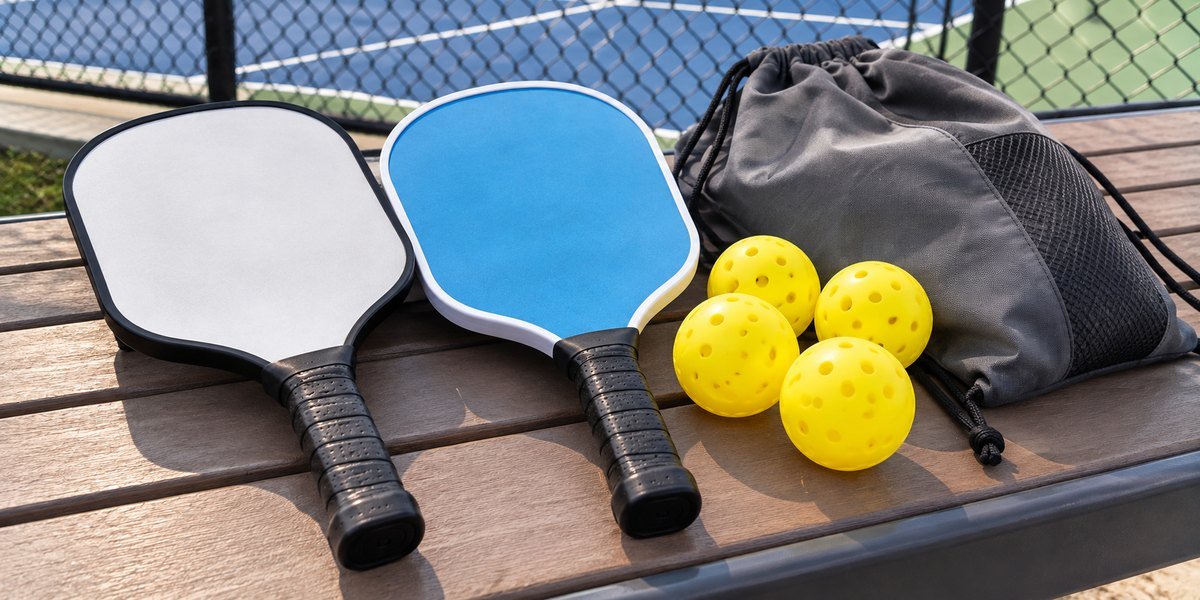 Two pickleball paddles, four balls and a drawstring bag on a bench
