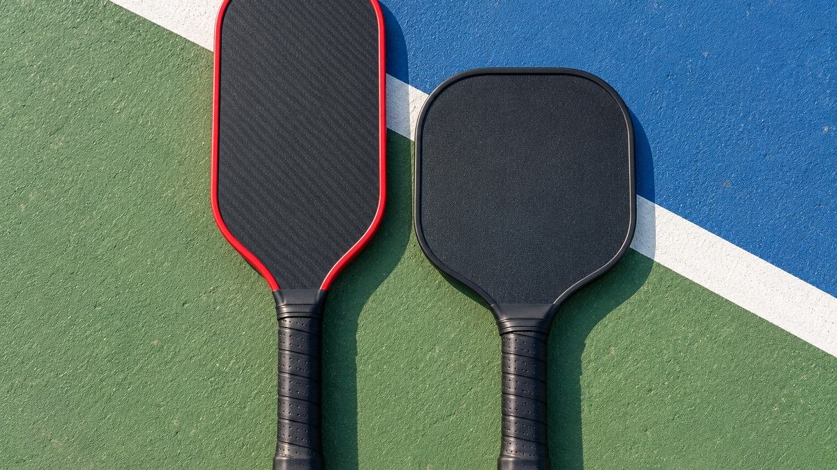 Elongated paddle with a red edge next to a standard paddle on a court